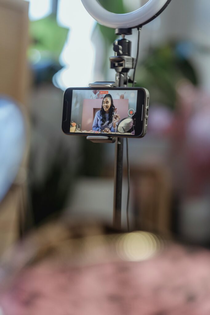 Woman using smartphone on tripod for vlogging tutorial indoors.